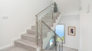 Eine moderne Treppe mit Glastrennlämmern und Holzstufen, die zu einem Balkon mit Meerblick führt.