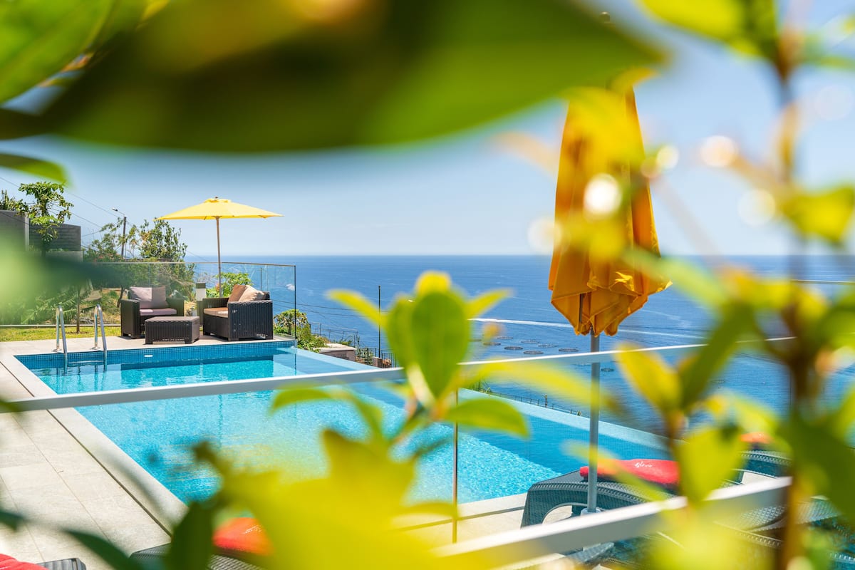 Ein Schwimmbecken mit Liegestühlen und Sonnenschirmen mit Blick auf ein Gewässer.