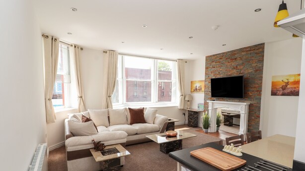 A modern living room with a sofa, a coffee table, a fireplace, and a kitchen area with a stove.