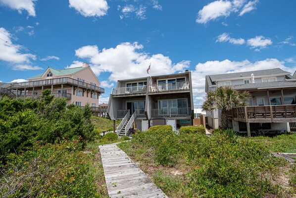 A beachfront property with a wooden boardwalk leading to a building with multiple balconies and a flag. - Bev's Beachfront Bungalow (Atlantic Beach)