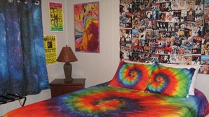 A bedroom with a colorful tie-dye bedspread, posters on the wall, and a cluttered bulletin board.