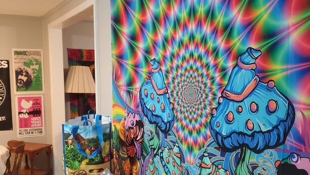 A room with a psychedelic wall mural, posters, and a wooden table.