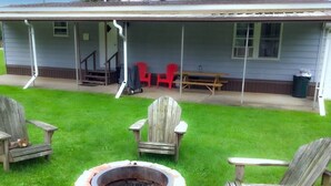 A backyard with a fire pit, wooden chairs, and a covered porch with red chairs and a table.
