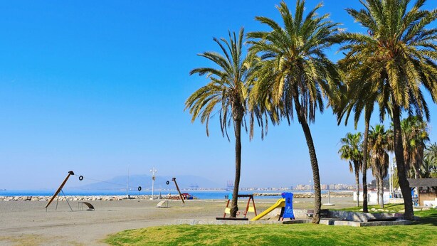 Una playa con palmeras, columpios y un parque infantil.