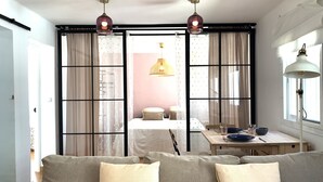 Una sala moderna con sofá, una mesa de comedor con platos y vasos, y un ventanal con cortinas.