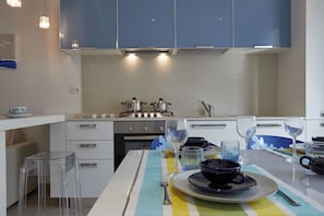 A modern kitchen with white cabinets, stainless steel appliances, and a striped tablecloth. - Casa Vivian SicilyMyHome (Pozzallo)