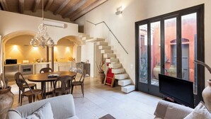 Un grand espace de vie comprenant une table à manger, un canapé et un téléviseur. Un escalier mène à un balcon d’où l’on a vue sur la rue.