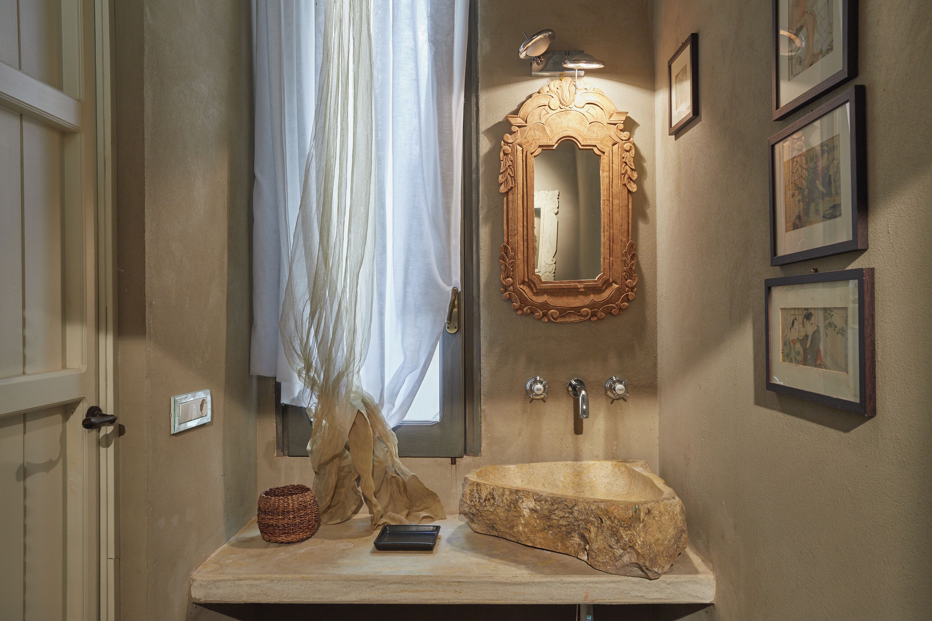 A bathroom with a stone sink, a mirror, and framed pictures on the wall.
