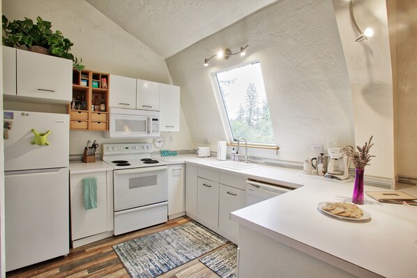 Enjoy cooking in this well-equipped kitchen with a central island, sink, and large window offering a view of the surrounding greenery.