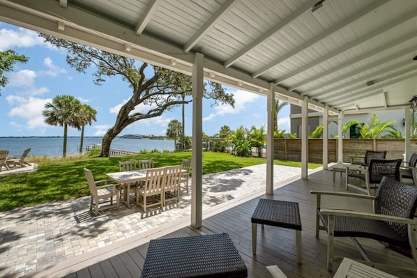 A covered outdoor patio with tables and chairs, a view of the water, and a large tree.