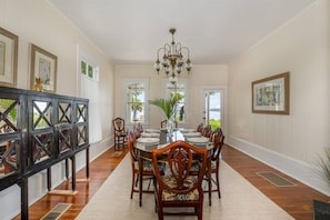 A dining room with a long table, chairs, a chandelier, and framed artwork on the walls.