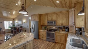 A spacious kitchen with wooden cabinets, granite countertops, stainless steel appliances, and pendant lighting. - 2 Docks 2 Shores- Ramp, Water Toys, Game Room! (Garrison)