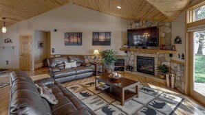 A spacious living room with a stone fireplace, leather sofas, and a large TV. - 2 Docks 2 Shores- Ramp, Water Toys, Game Room! (Garrison)