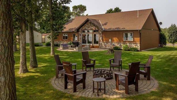 Une maison avec des fondations en pierre, un revêtement extérieur en bois et un patio circulaire agrémenté de chaises et d’un foyer.