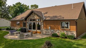 Une maison moderne avec une façade en pierre, de grandes fenêtres et un patio aménagé avec du mobilier d’extérieur.