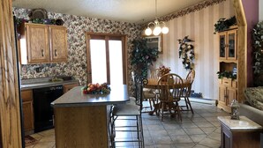 A kitchen with wooden cabinets, a dining table with chairs, and a tiled floor. - Spacious home, large deck with beautiful views in the heart of the Black Hills  (Rapid City)