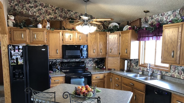 A kitchen with wooden cabinets, a black refrigerator, a microwave, a stove, and a dining area with two chairs and a table. - Spacious home, large deck with beautiful views in the heart of the Black Hills  (Rapid City)
