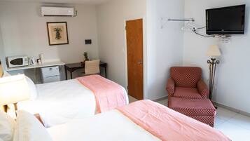 A hotel room with two beds, a desk, a chair, a TV, and a lamp.
