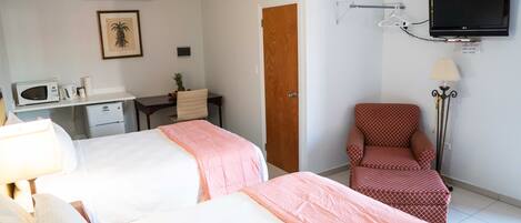 A hotel room with two beds, a desk, a chair, a TV, and a lamp.