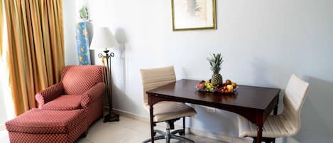 A room with a dining table, two chairs, a red armchair, a lamp, and a framed picture on the wall.
