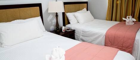 Habitación de hotel con dos camas, cada una con ropa de cama blanca y un toque de color rosa. Se observan cuadros en la pared y una lámpara en la mesita de noche.