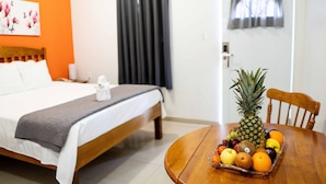 A hotel room with a bed, a wooden table with a fruit basket, and a window with curtains. - The Paradise Inn (Philipsburg)