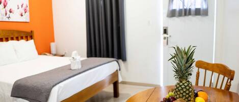 Una habitación de hotel con cama, una mesa de madera con una cesta de fruta y una ventana con cortinas.