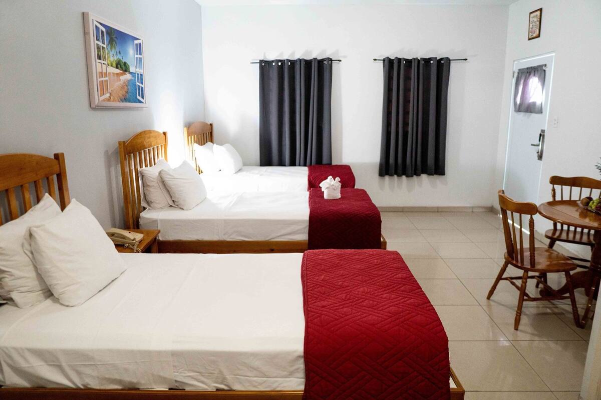 A hotel room with two beds, a dining table with chairs, and a painting on the wall.