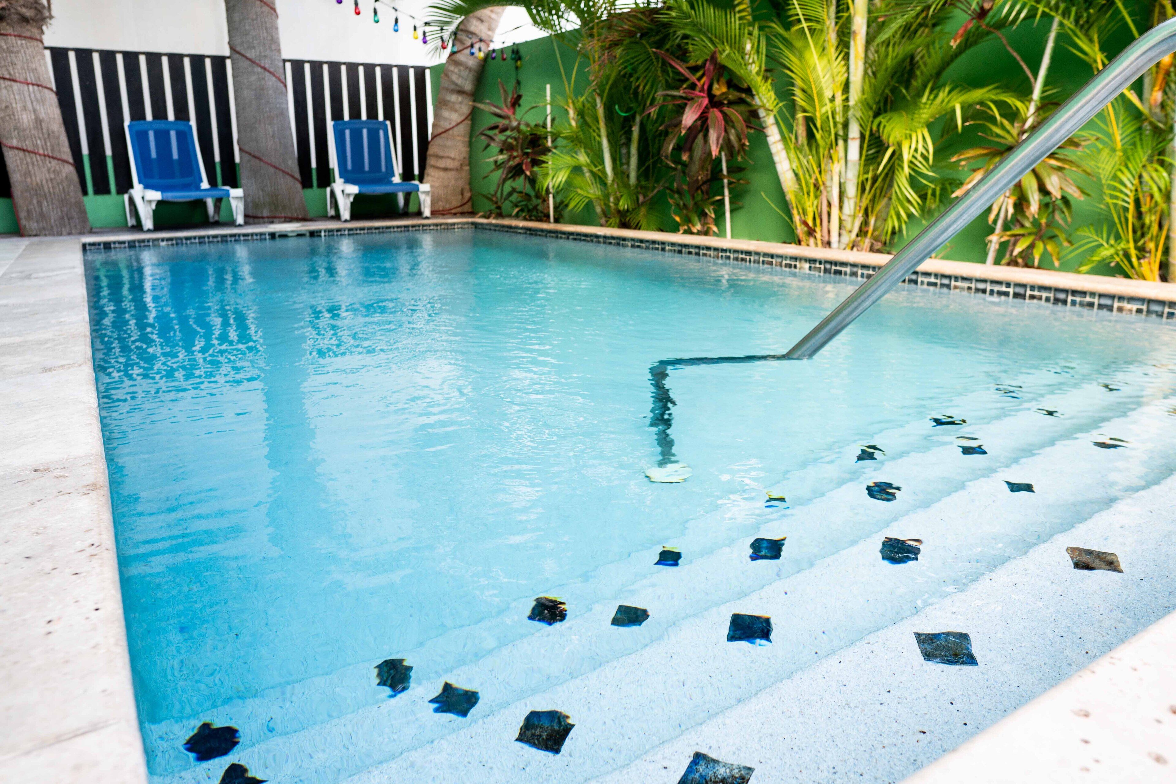 A swimming pool with clear blue water, steps leading into the pool, and a few lounge chairs by the poolside. - The Paradise Inn (Philipsburg)