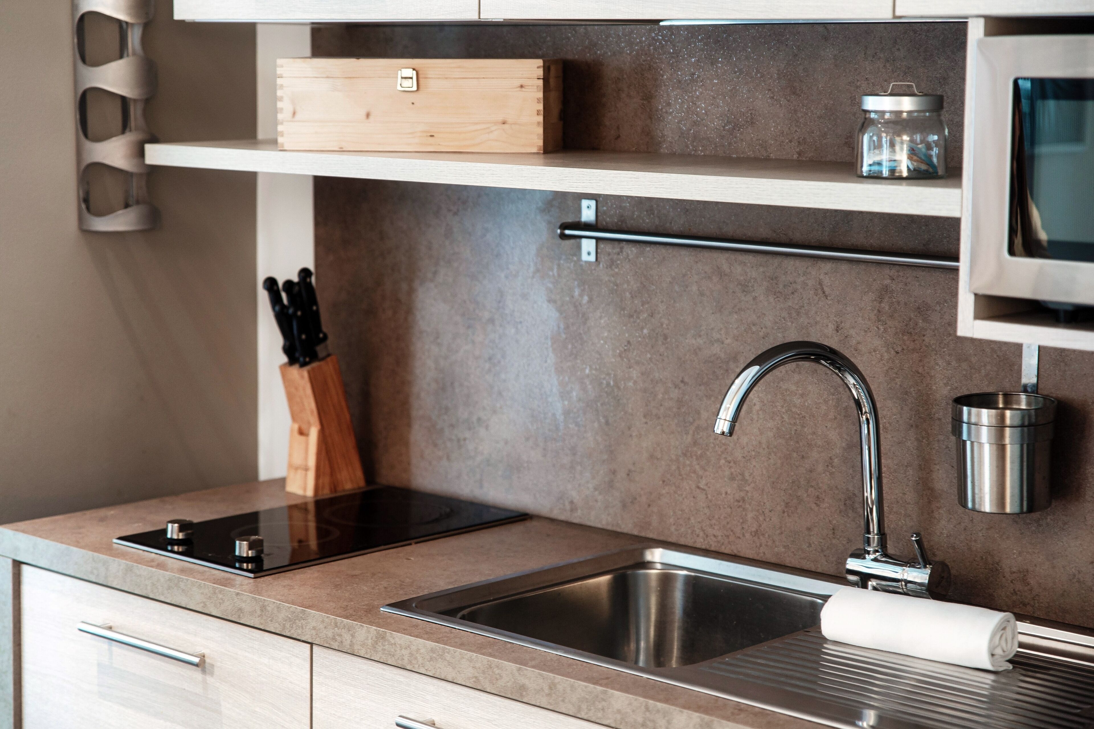 A modern kitchen with a stainless steel sink, a built-in stove, and a wooden box on a shelf.