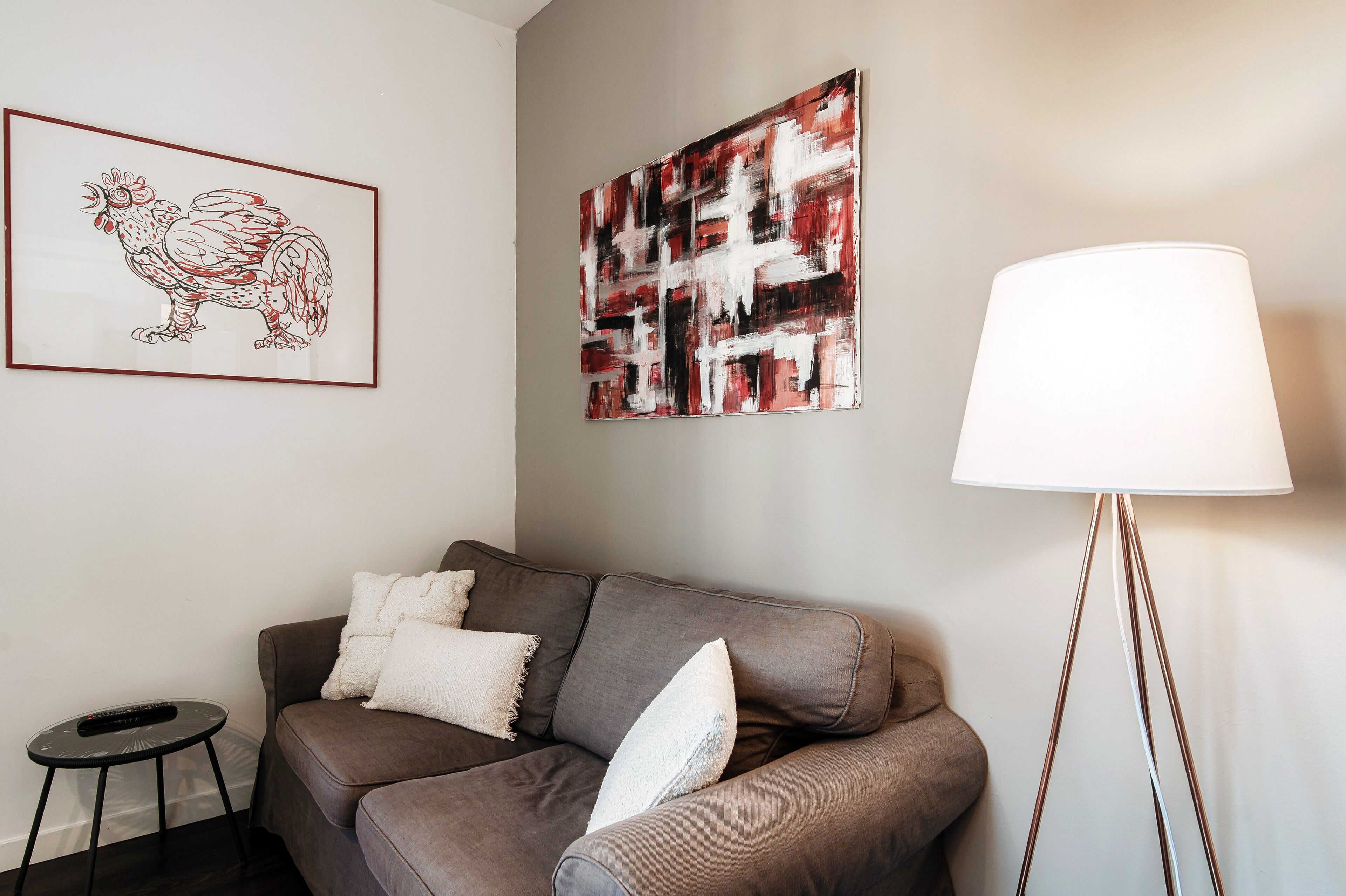 A living room with a brown sofa, a framed rooster artwork, an abstract painting, and a floor lamp.