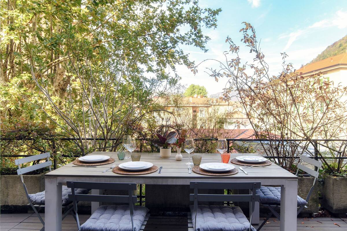 A dining table set outdoors with chairs, plates, glasses, and cutlery.