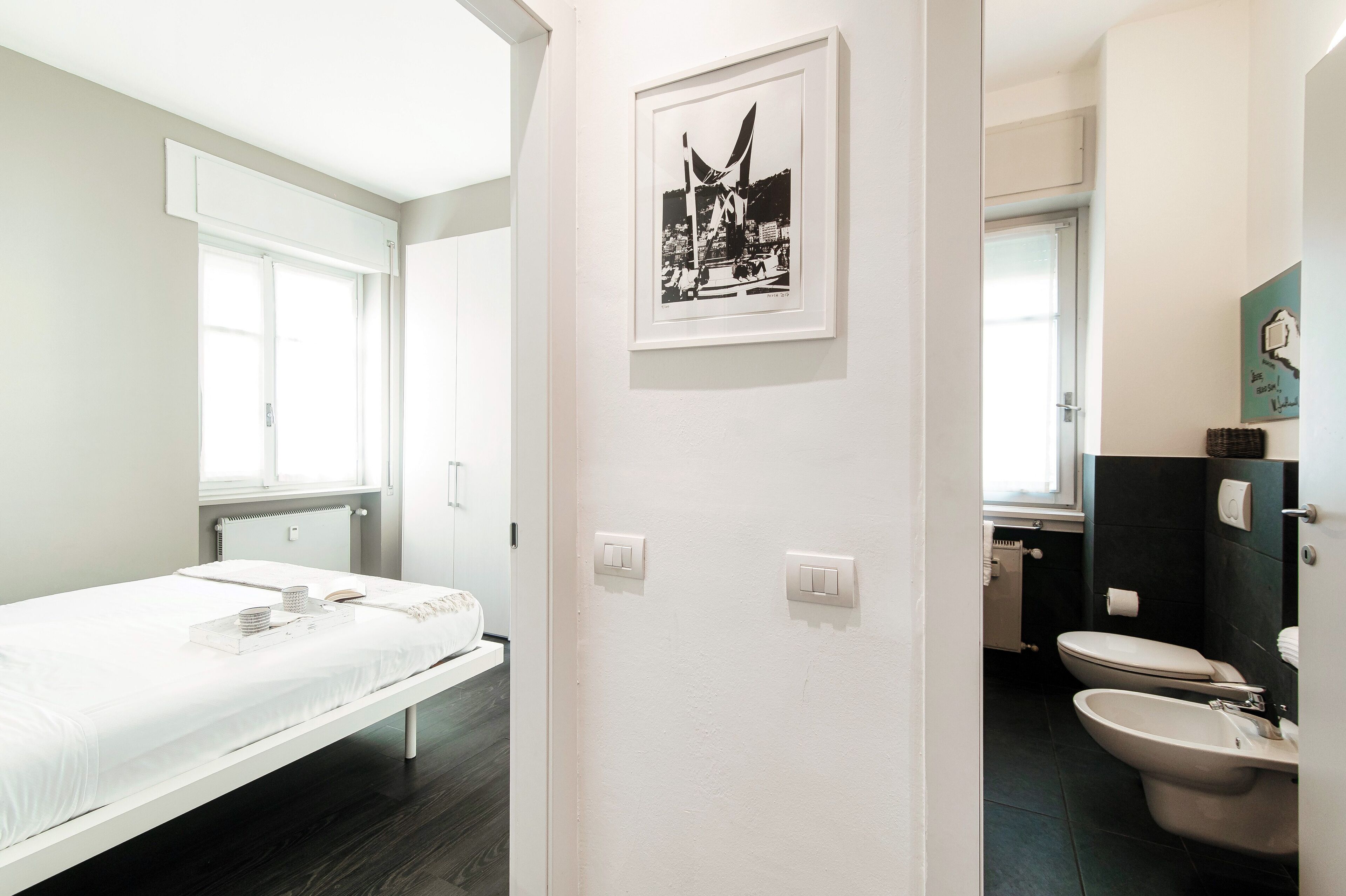 Una habitación de hotel moderna con cama, baño con inodoro y lavamanos, y un cuadro en la pared.