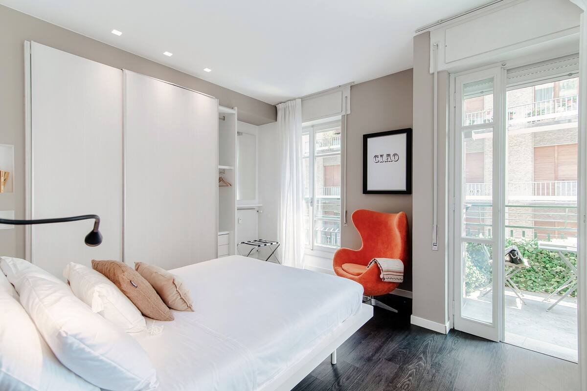 A modern bedroom with a large bed, a bright window, and a balcony.