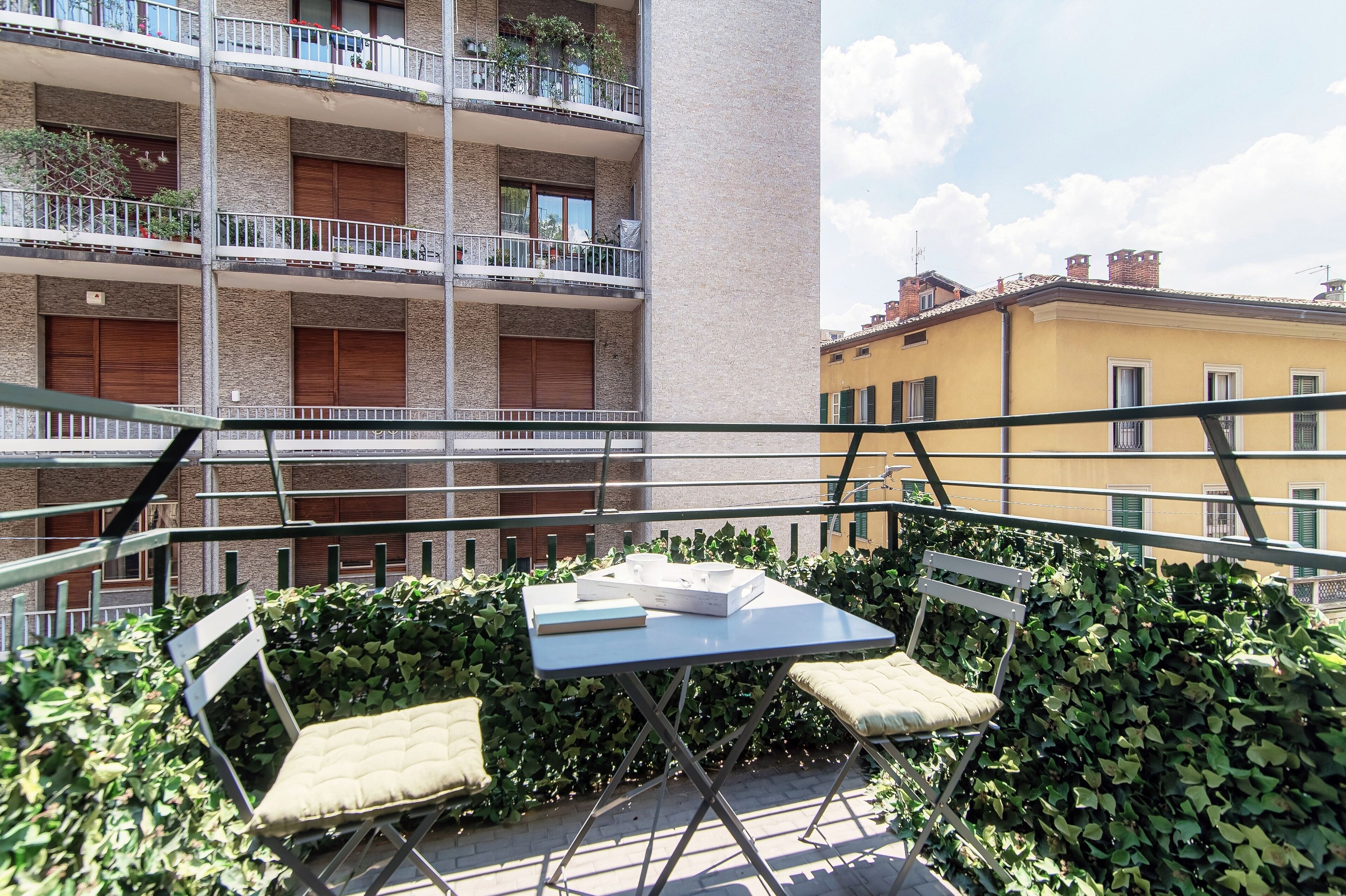 Een balkon met een tafel en twee stoelen, omgeven door groen.