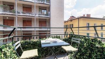 Een balkon met een tafel en twee stoelen, omgeven door groen.