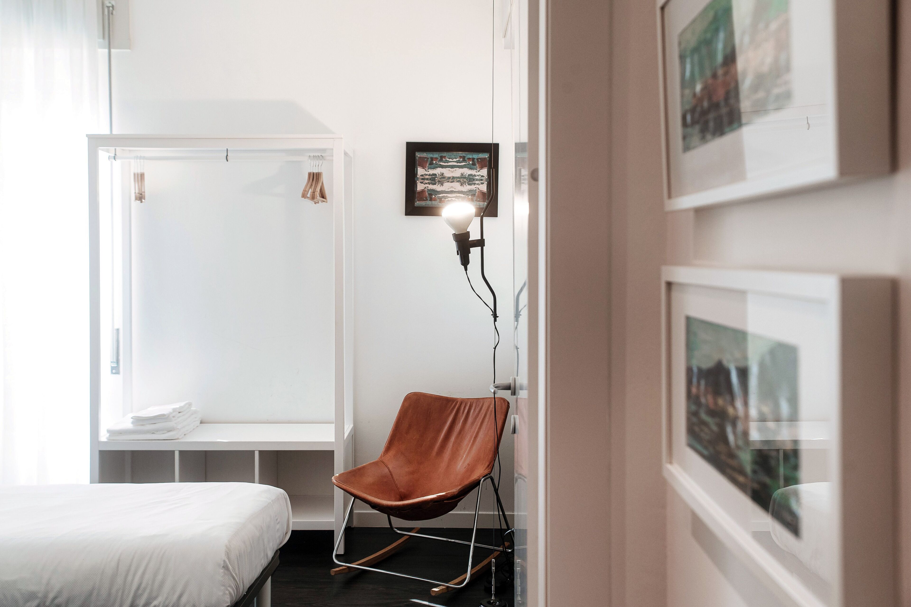 Un dormitorio con una cama, un armario blanco, una silla marrón y cuadros enmarcados en la pared.