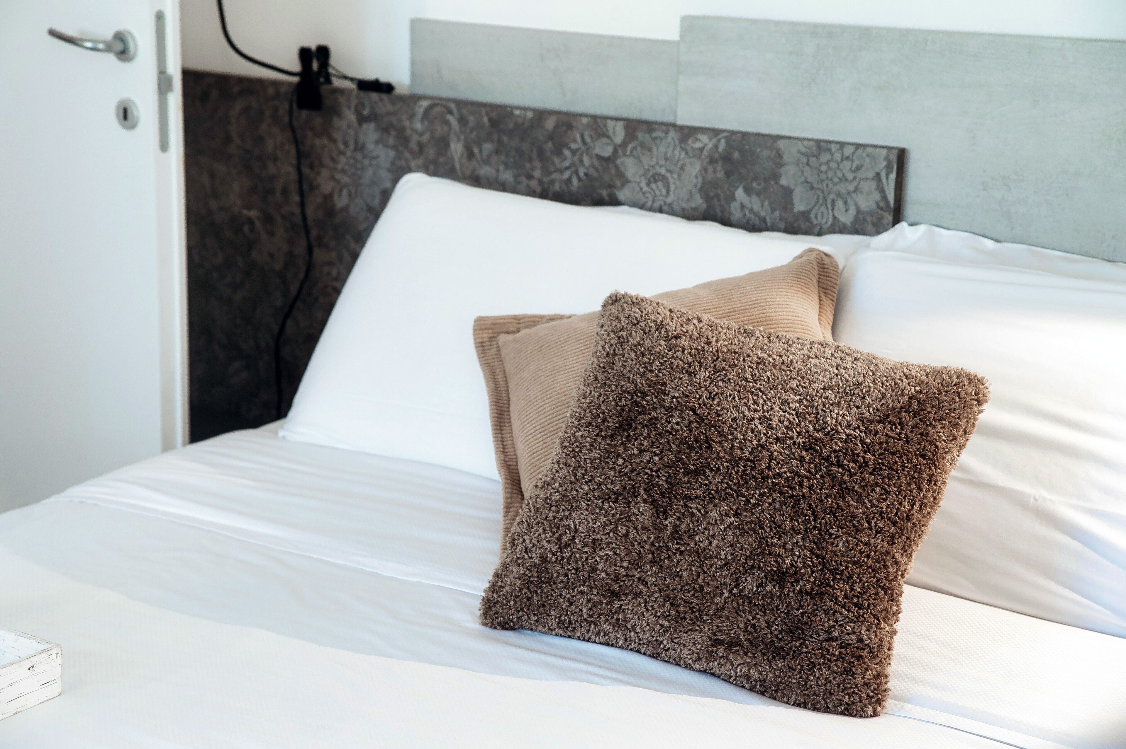 Una cama bien hecha con sábanas blancas y dos almohadas marrones.