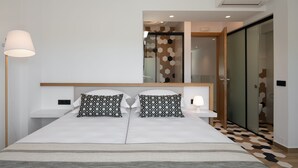 A modern hotel room with a large bed, two patterned pillows, a bedside table with a lamp, and a view of a bathroom through a glass door. - De.Light Boutique Villa II, close to Rethymno (Atsipopoulo)