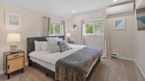Un dormitorio con cama, dos mesitas de noche y dos ventanas con cortinas.