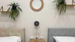 A hotel room with two beds, a small wooden side table, a wall-mounted mirror, and two hanging plants.