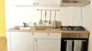 A compact kitchen with a sink, stove, oven, and hanging utensils.