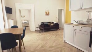 A spacious living area with a dining table and chairs, a sofa, and a kitchen area with cabinets and a sink.