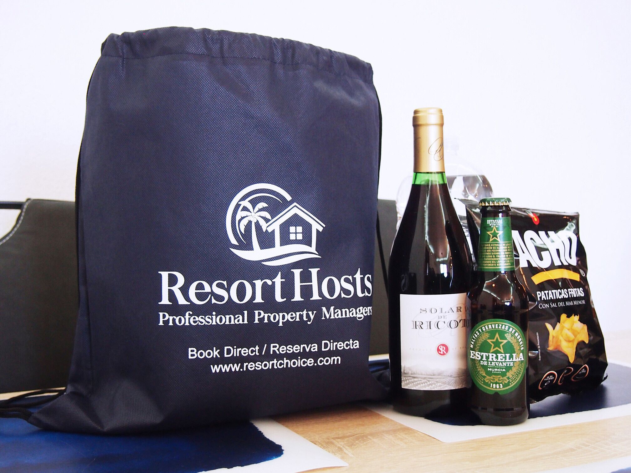 A bag with a logo, a bottle of wine, a bottle of beer, and a bag of chips.