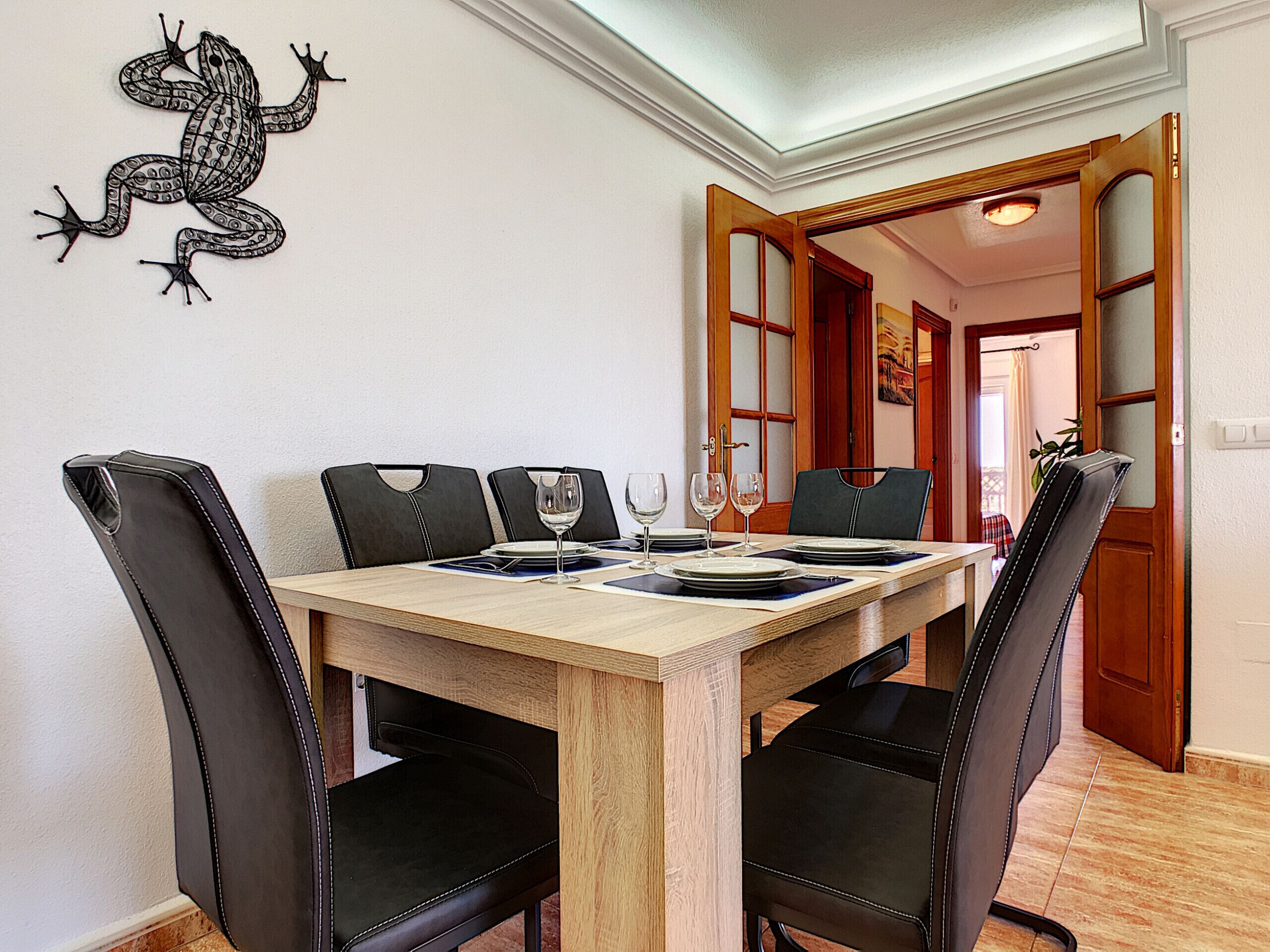 A dining area with a wooden table, black upholstered chairs, and a decorative wall piece.