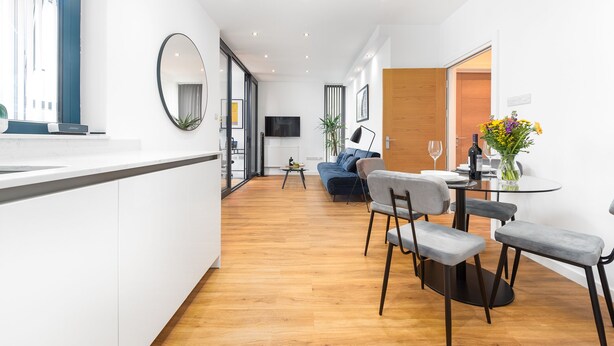 Una sala de estar moderna con un sofá, una mesa de comedor con sillas, un televisor y un ventanal grande.