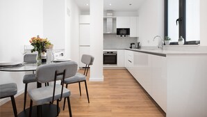 Una cocina moderna con armarios blancos, una isla central y un comedor con mesa de vidrio y sillas grises.