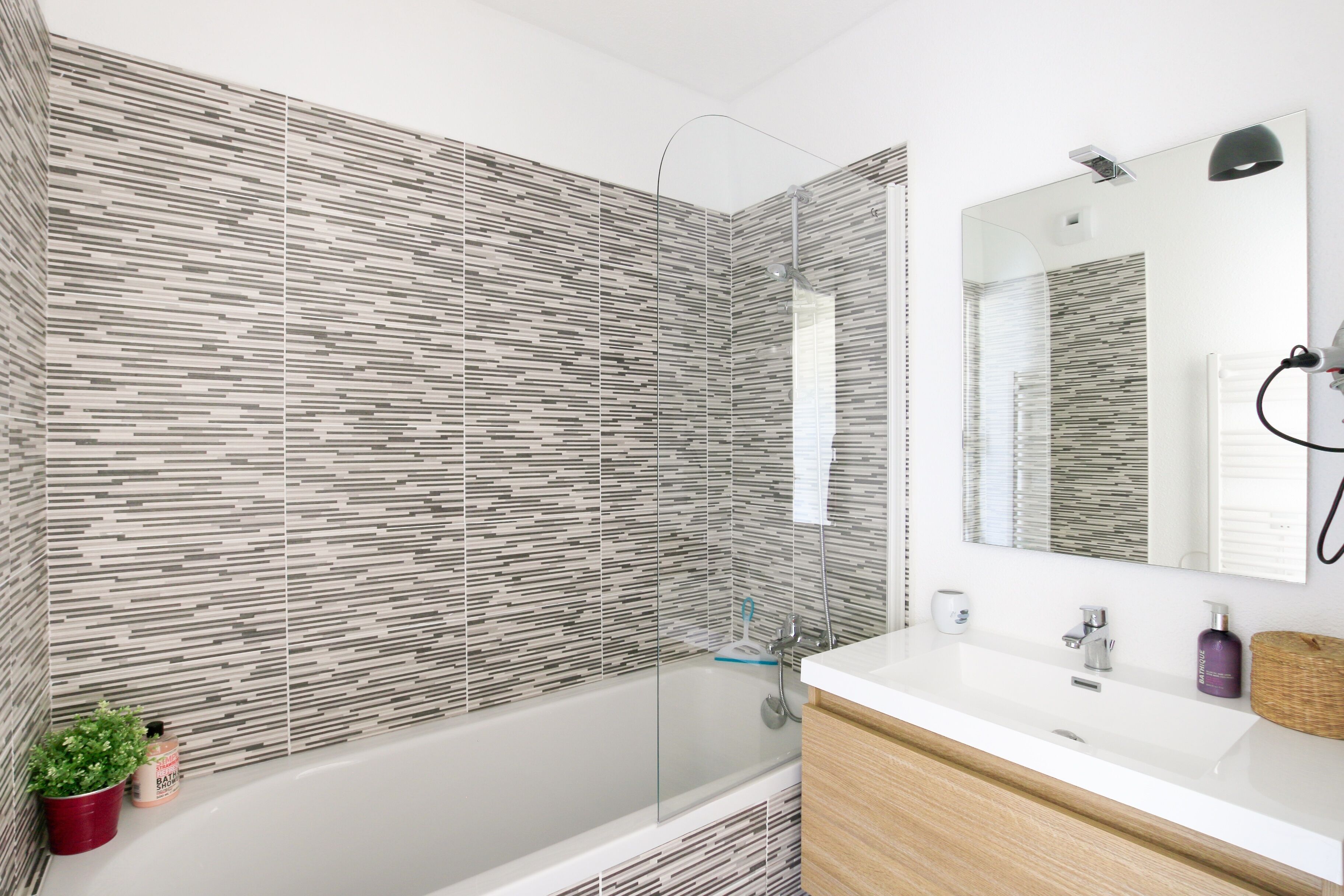 A modern bathroom with a glass-enclosed shower, a white sink, and a wooden vanity.