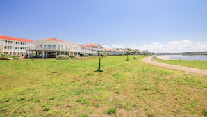 Un hôtel situé sur la côte, avec un bâtiment à toit rouge, une pelouse verdoyante et un sentier menant à la plage.