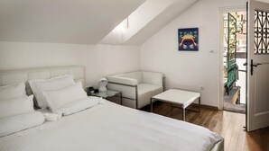 Een slaapkamer met een groot bed, een klein tafeltje, een bank en een deur naar een buitenruimte.